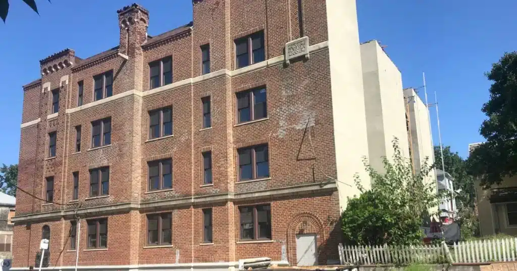 Four-story red brick apartment building under clear blue sky, managed by Realty Management Services.