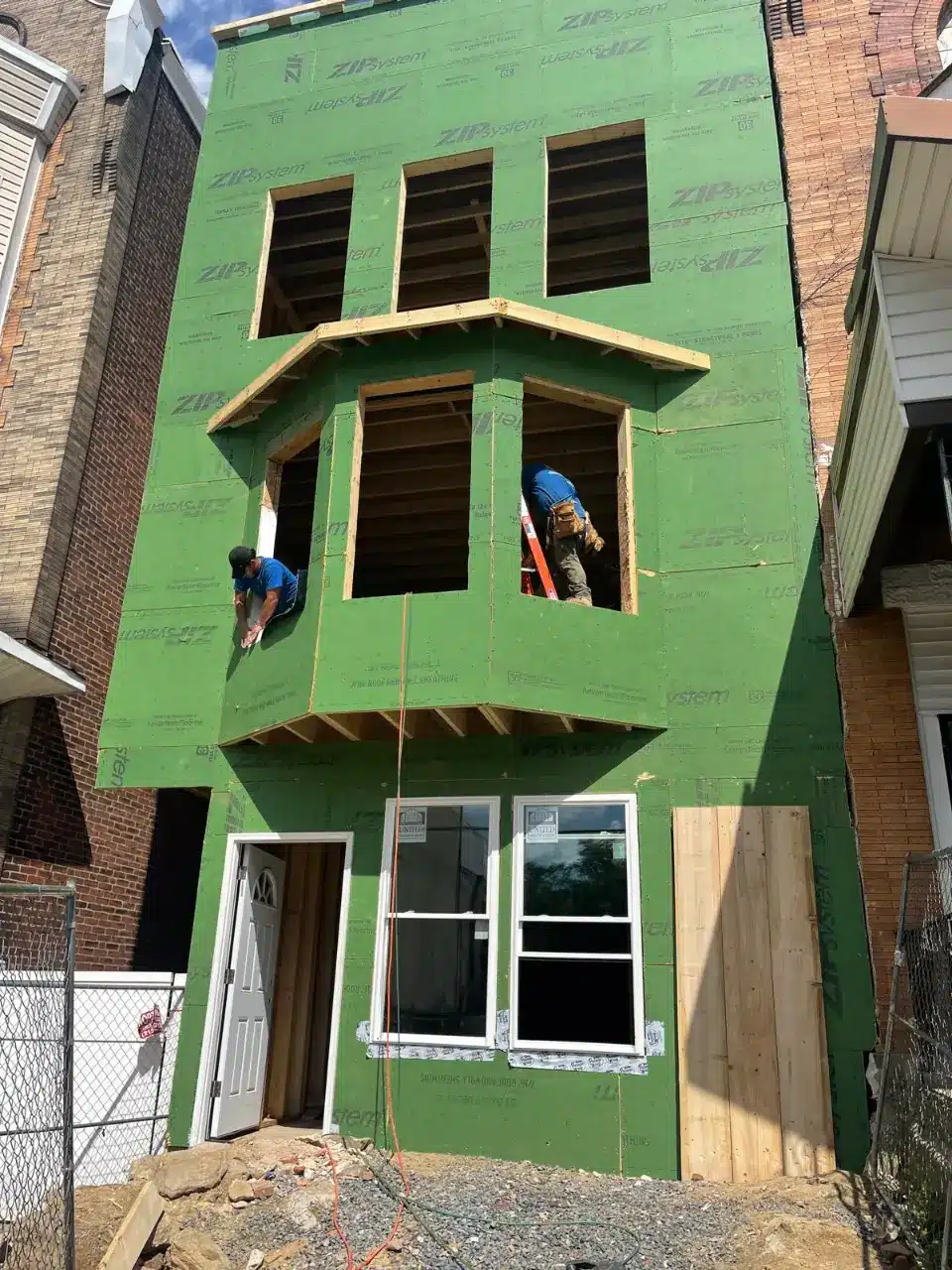 Construction workers installing framing on a green ZIP System house under renovation, part of realty management services provided