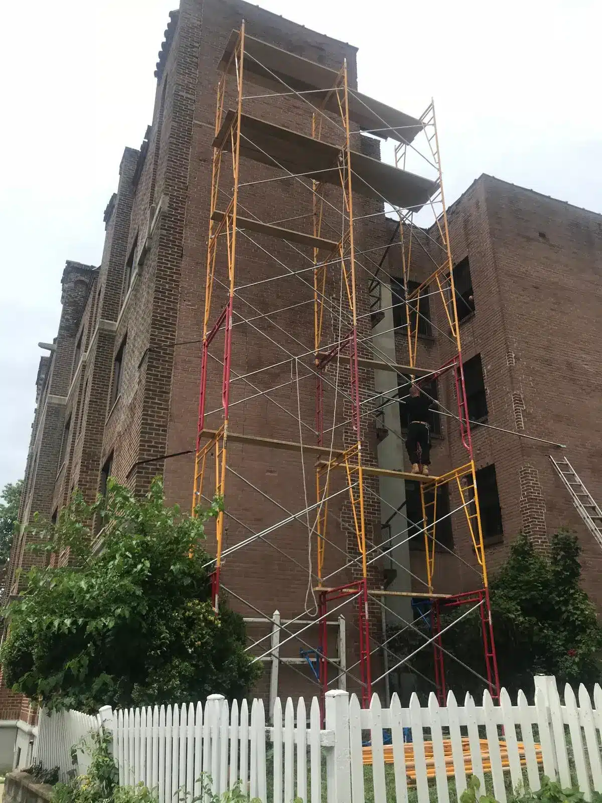 Scaffolding set up against a brick apartment building with a worker repairing the exterior, illustrating rental property insurance needs.